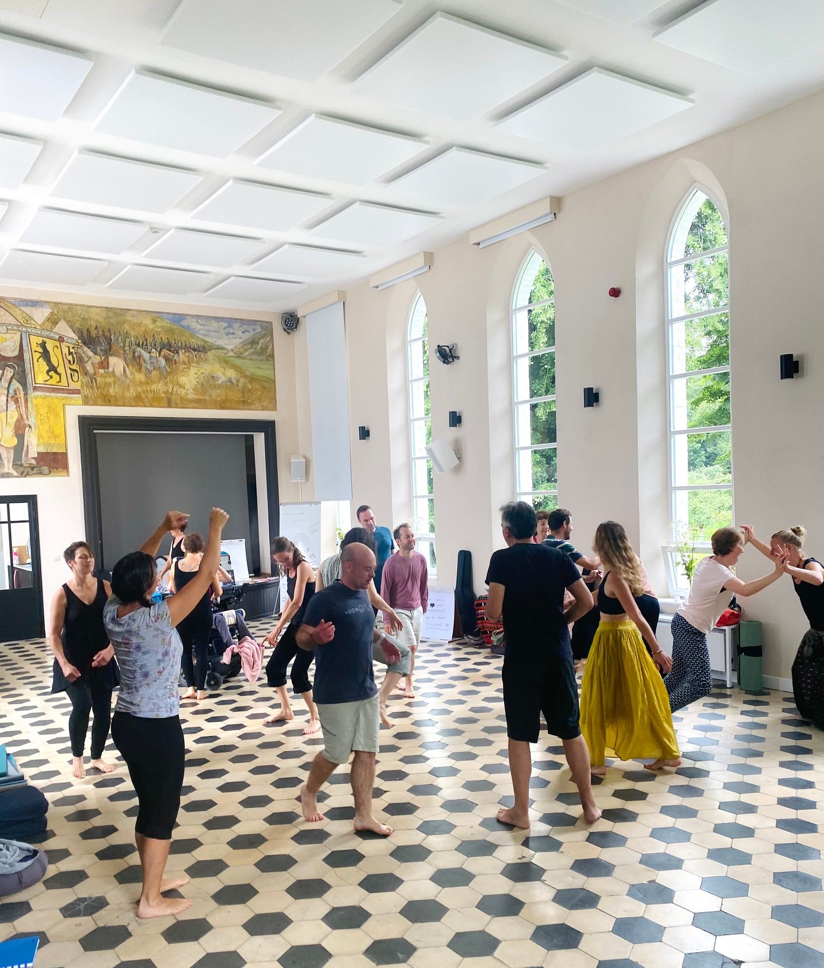 Group of people dancing barefoot in a bright room with large windows and hexagonal floor tiles.