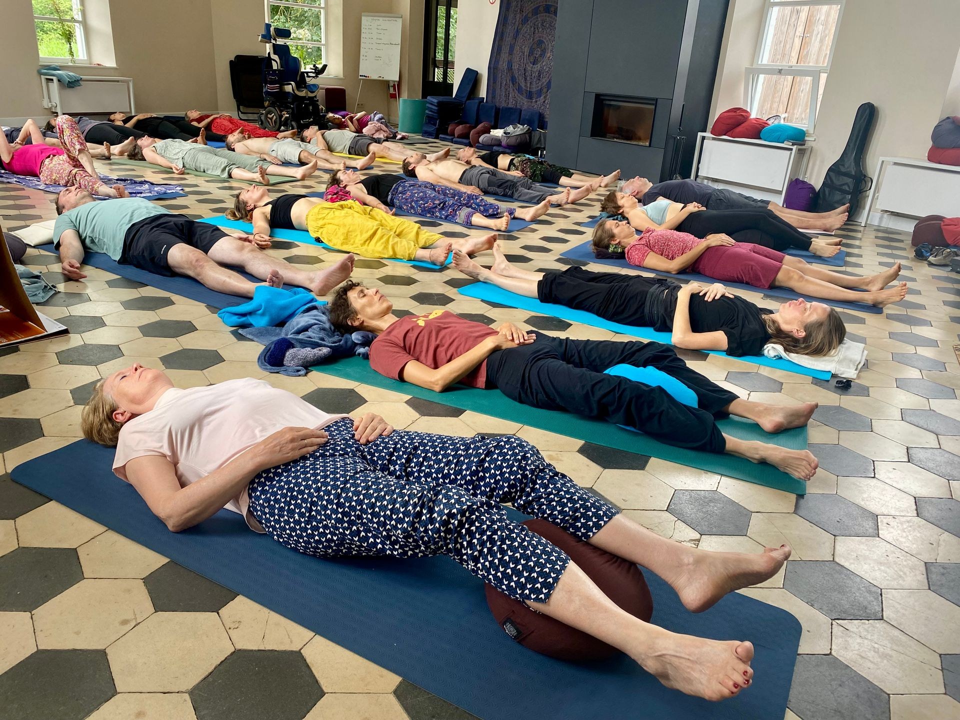 Group of people lying on yoga mats in a bright room, practicing relaxation or meditation.