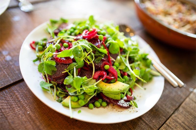 Colorful salad with greens, avocado, red onions, and peas on a white plate.