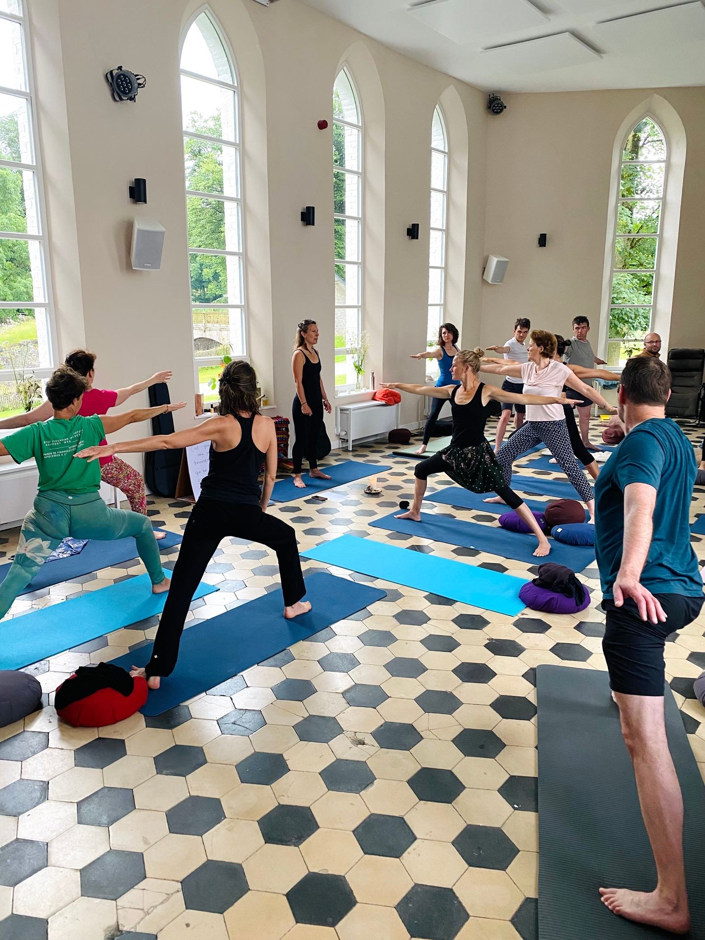 Group of people practicing yoga in a bright room with large windows and hexagonal floor tiles.