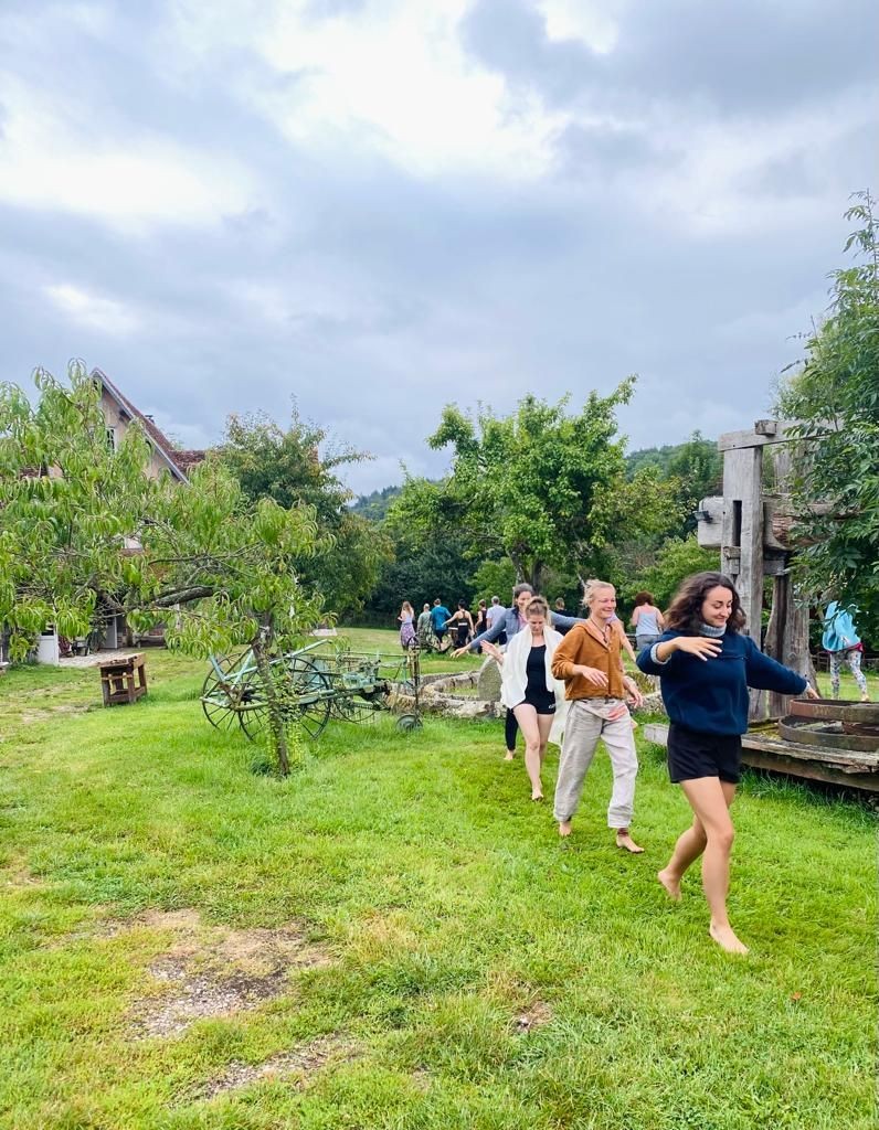 Group of people walking barefoot on a grassy field with trees and old machinery in the background.