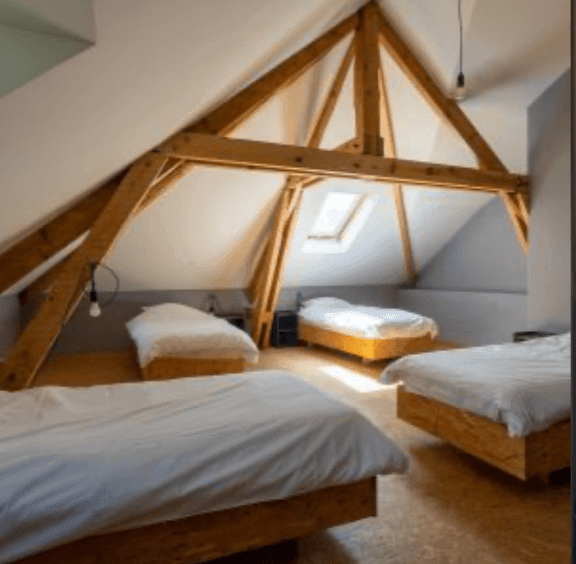 Attic bedroom with four wooden beds, exposed beams, and a skylight.