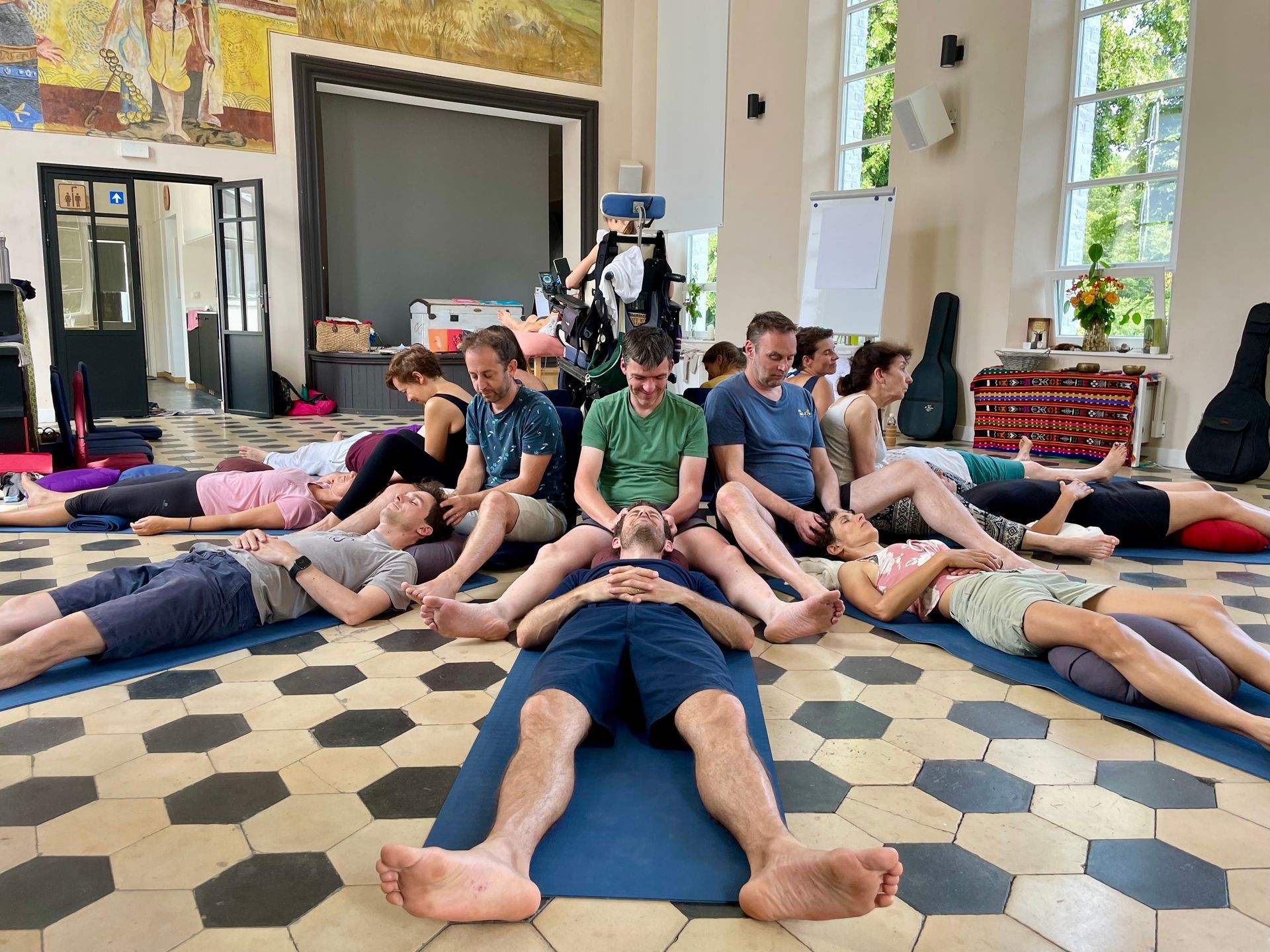 Group of people lying on yoga mats in a classroom, engaged in a relaxation or meditation session.